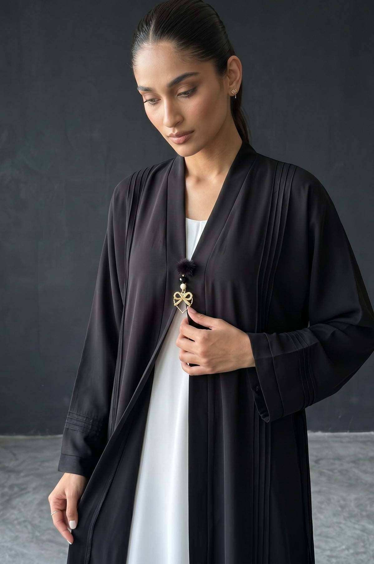 Styled front view of Monochrome Pleated Brooch Abaya showing vertical pintuck pleats