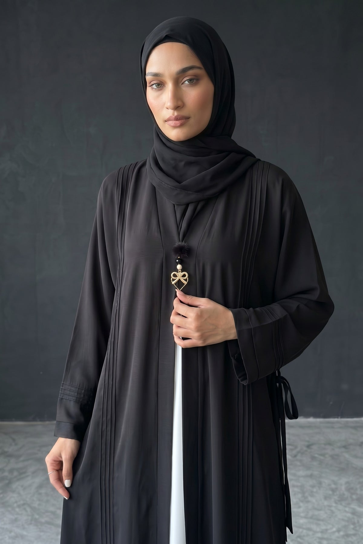 Close-up detail of Monochrome Pleated Brooch Abaya showcasing golden bow brooch hardware