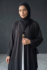 Close-up detail of Monochrome Pleated Brooch Abaya showcasing golden bow brooch hardware