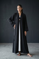 Full length standing view of Monochrome Pleated Brooch Abaya showing black and white color-block